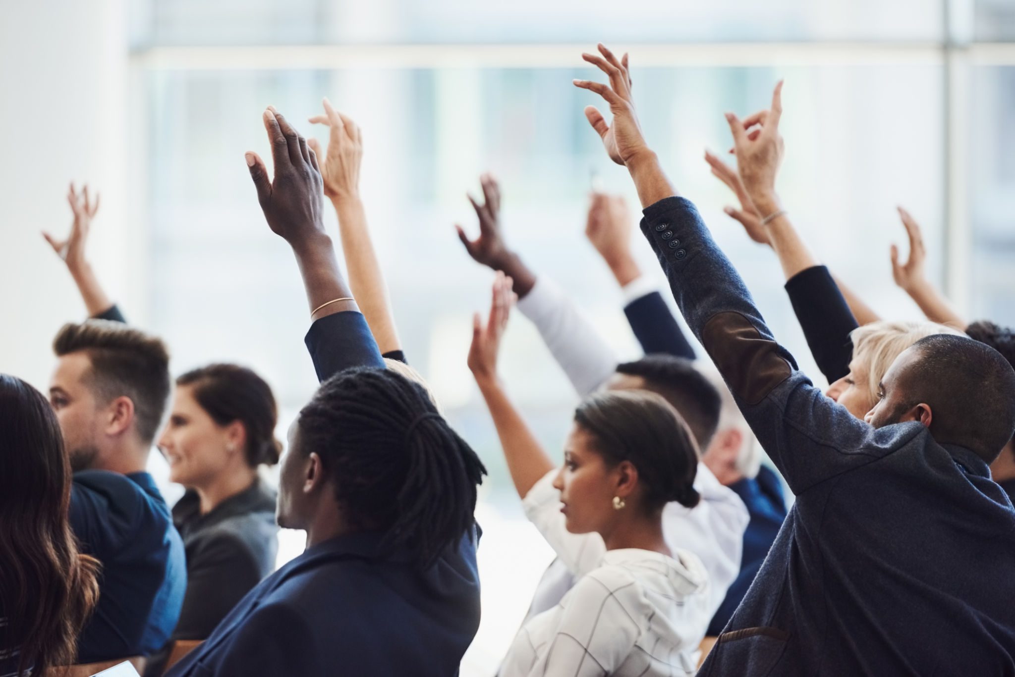 A diverse group of people raising their hands in a meeting.