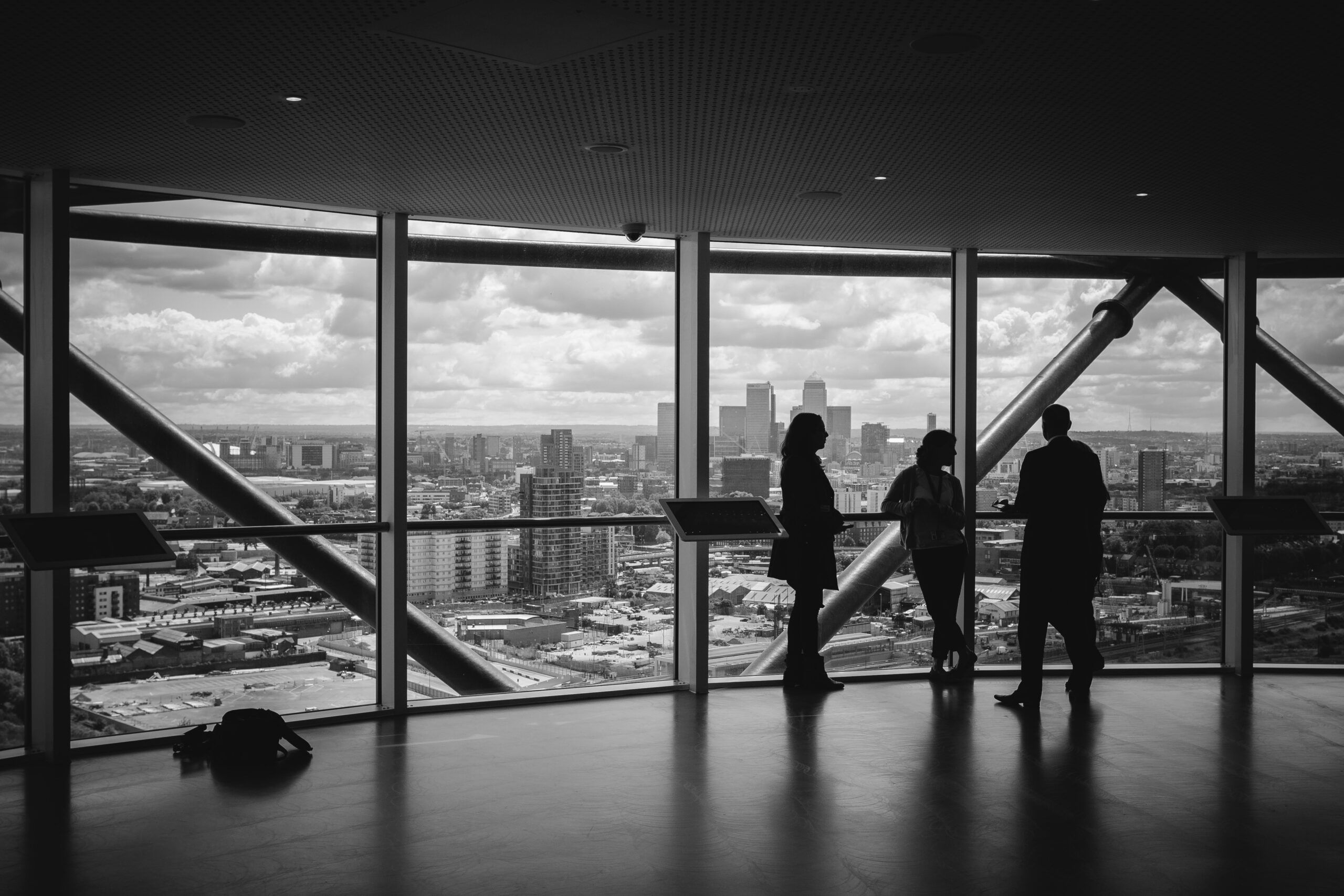 Silhouettes of people overlooking a city through large windows.
