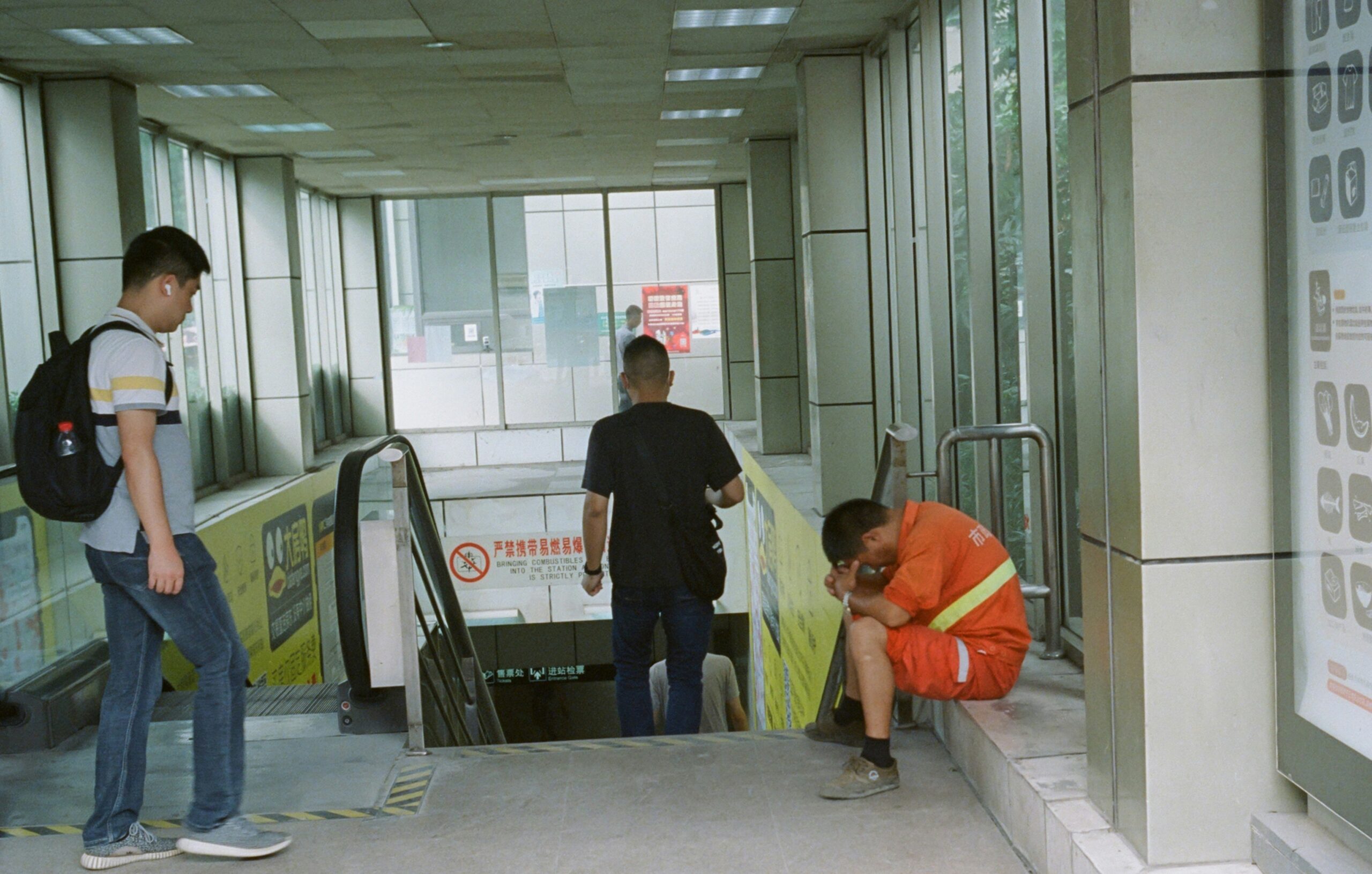 Man walking toward escalator while another person in orange rests nearby.
